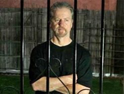 A man standing behind bars in front of a fence.